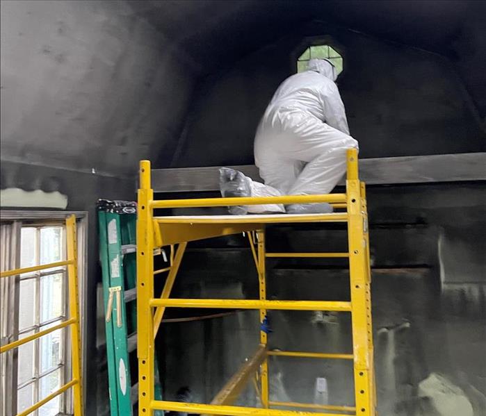 man in a white suit cleaning black charred up walls in the studio