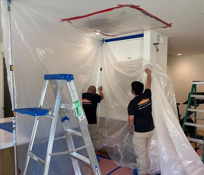 2 men setting up a plastic paper with white walls and ceilings 